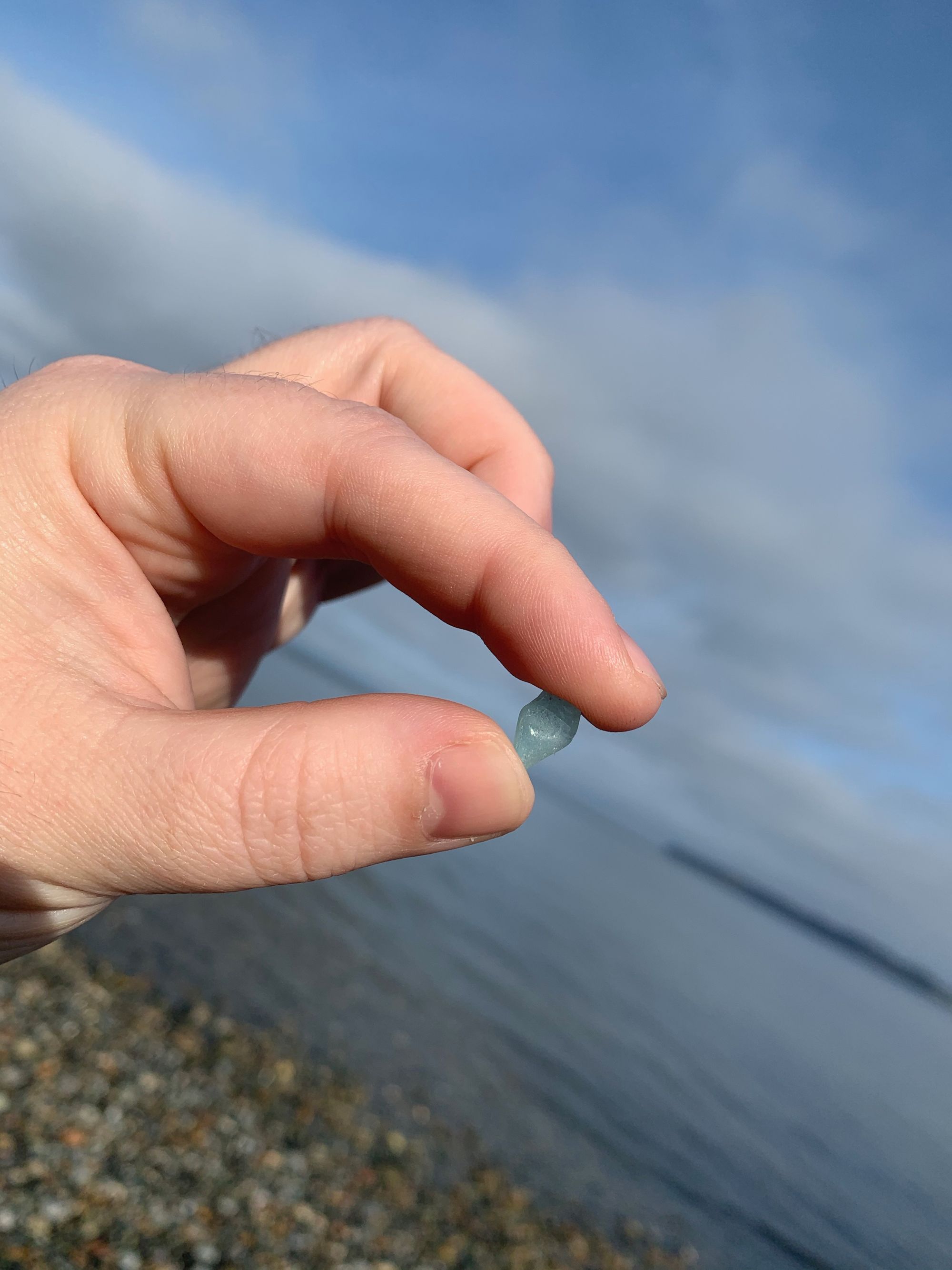 a small piece of blue seaglass held by a hand against a view of the beach