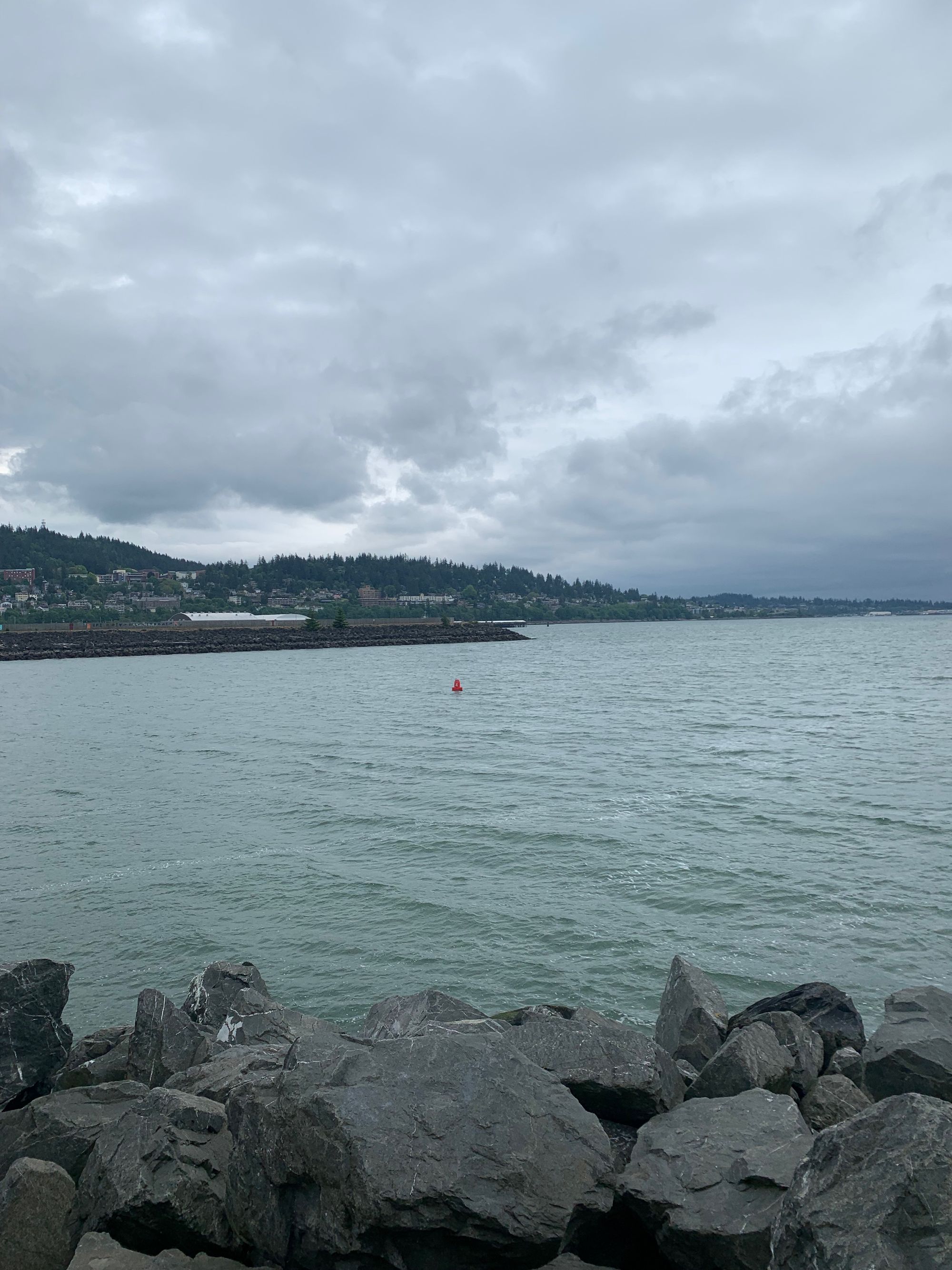 view of a bay with rocks in foreground & red buoy in the distance