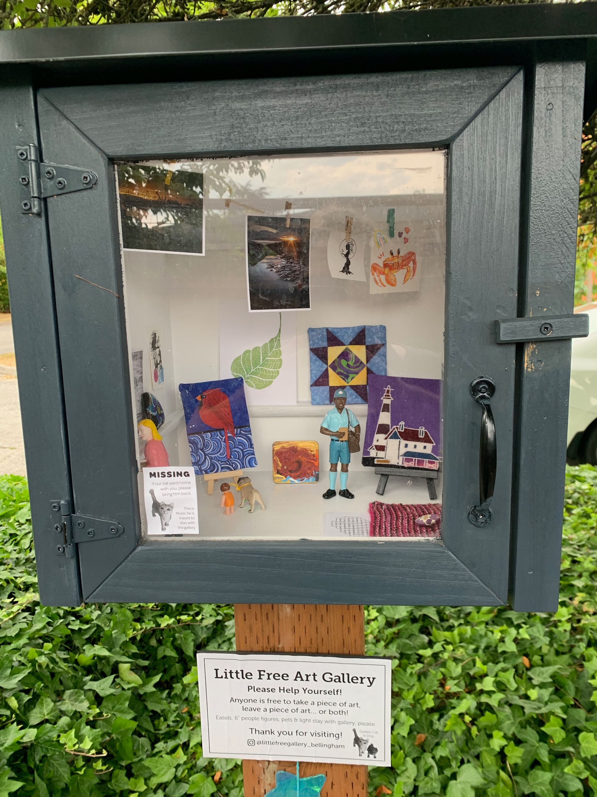 small grey wooden box with glass door holding tiny works of art