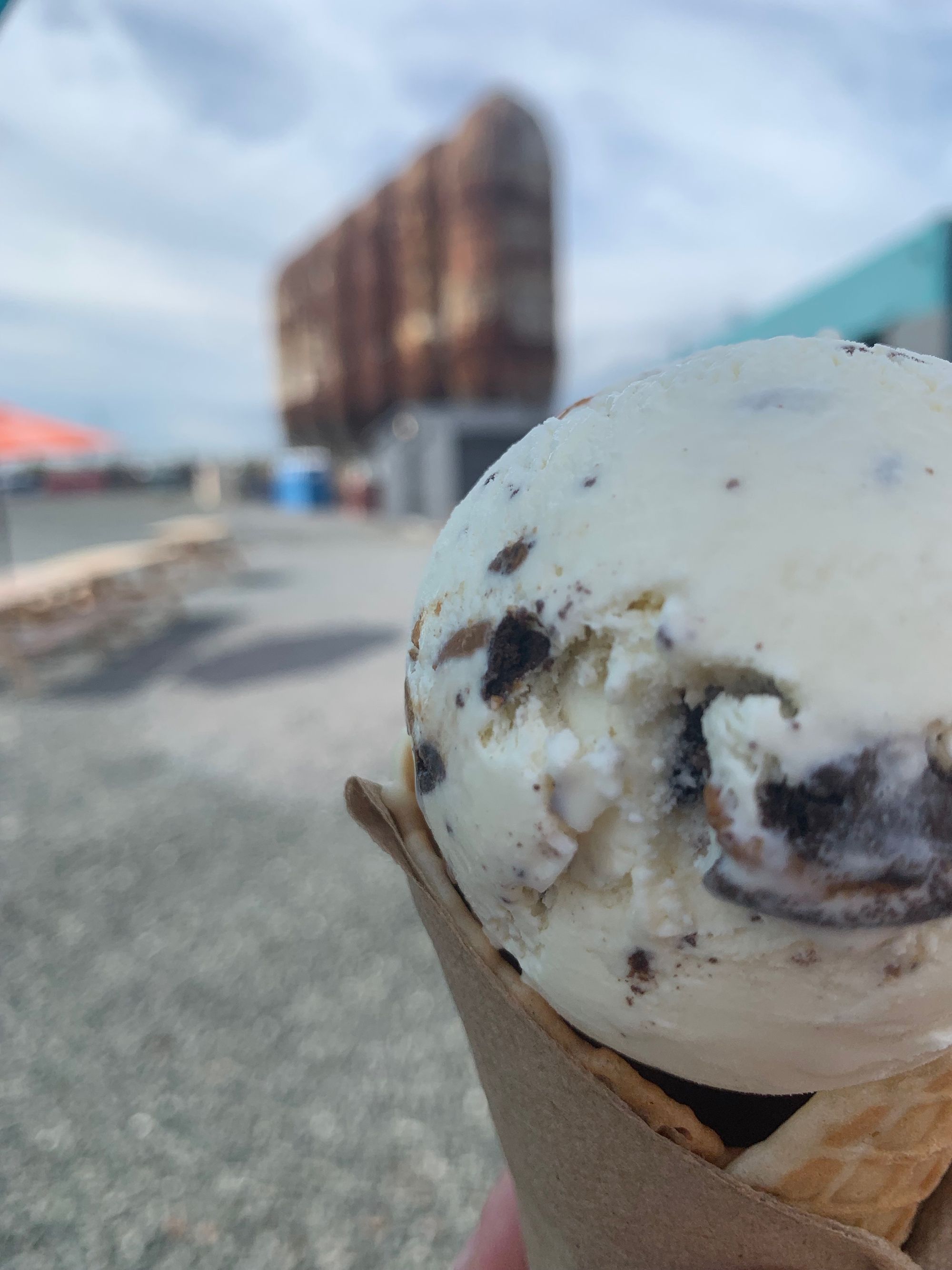 ice cream cone in foreground, industrial equipment against cloudy sky