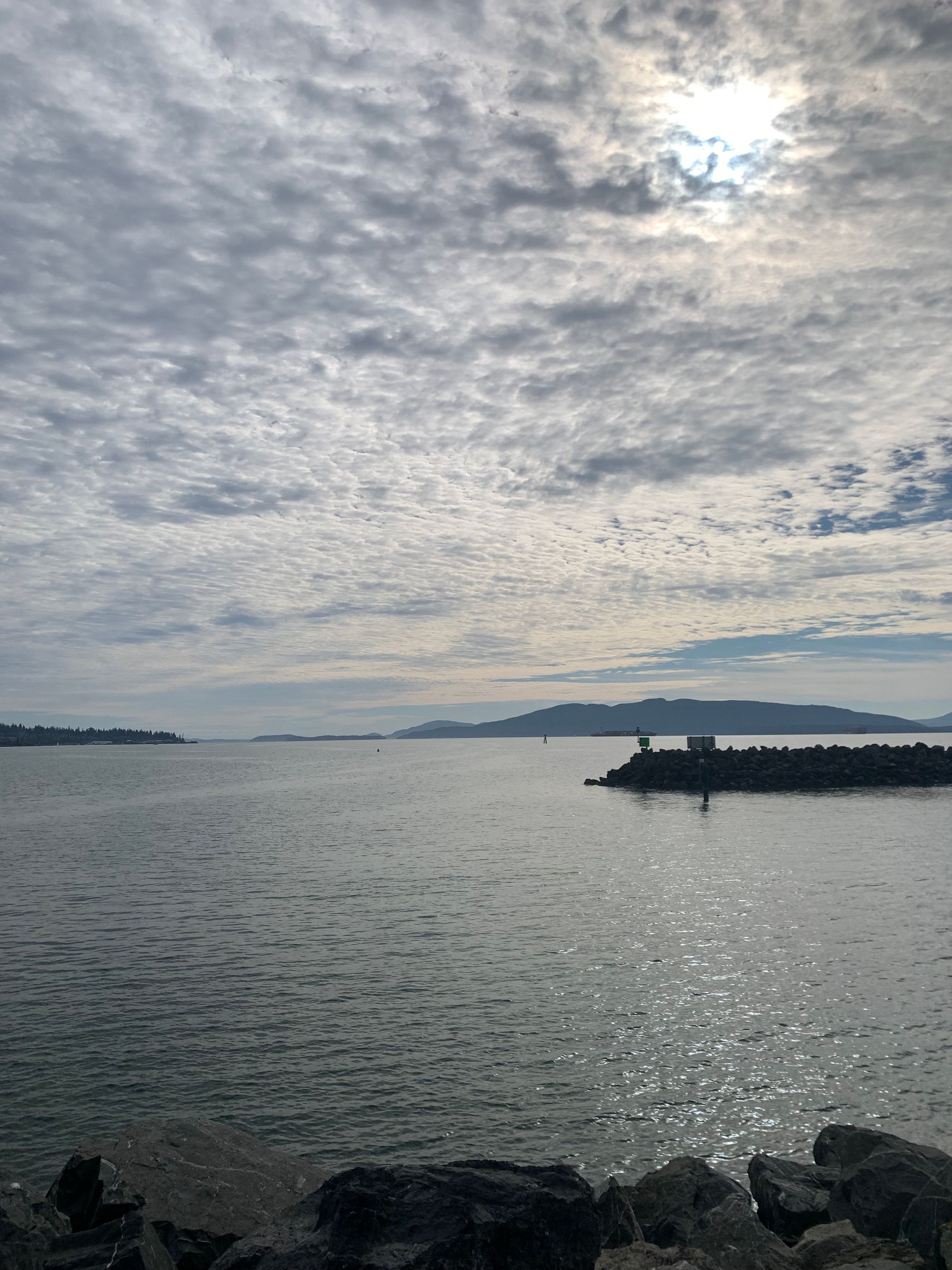 rocks in foreground, grey water, white clouds above