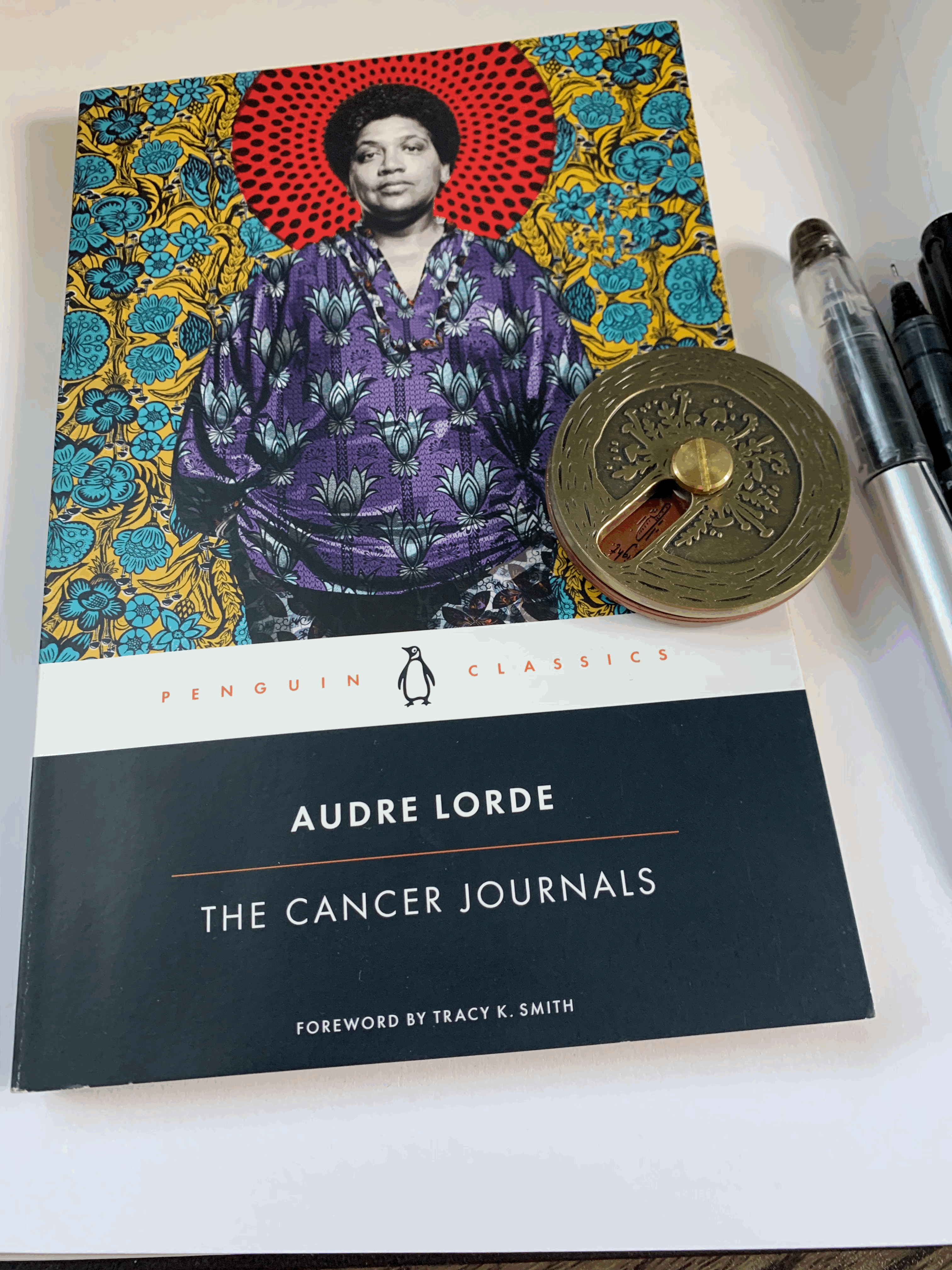 cover of Audio Lorde's the Cancer Journals, little round brass object, two pens