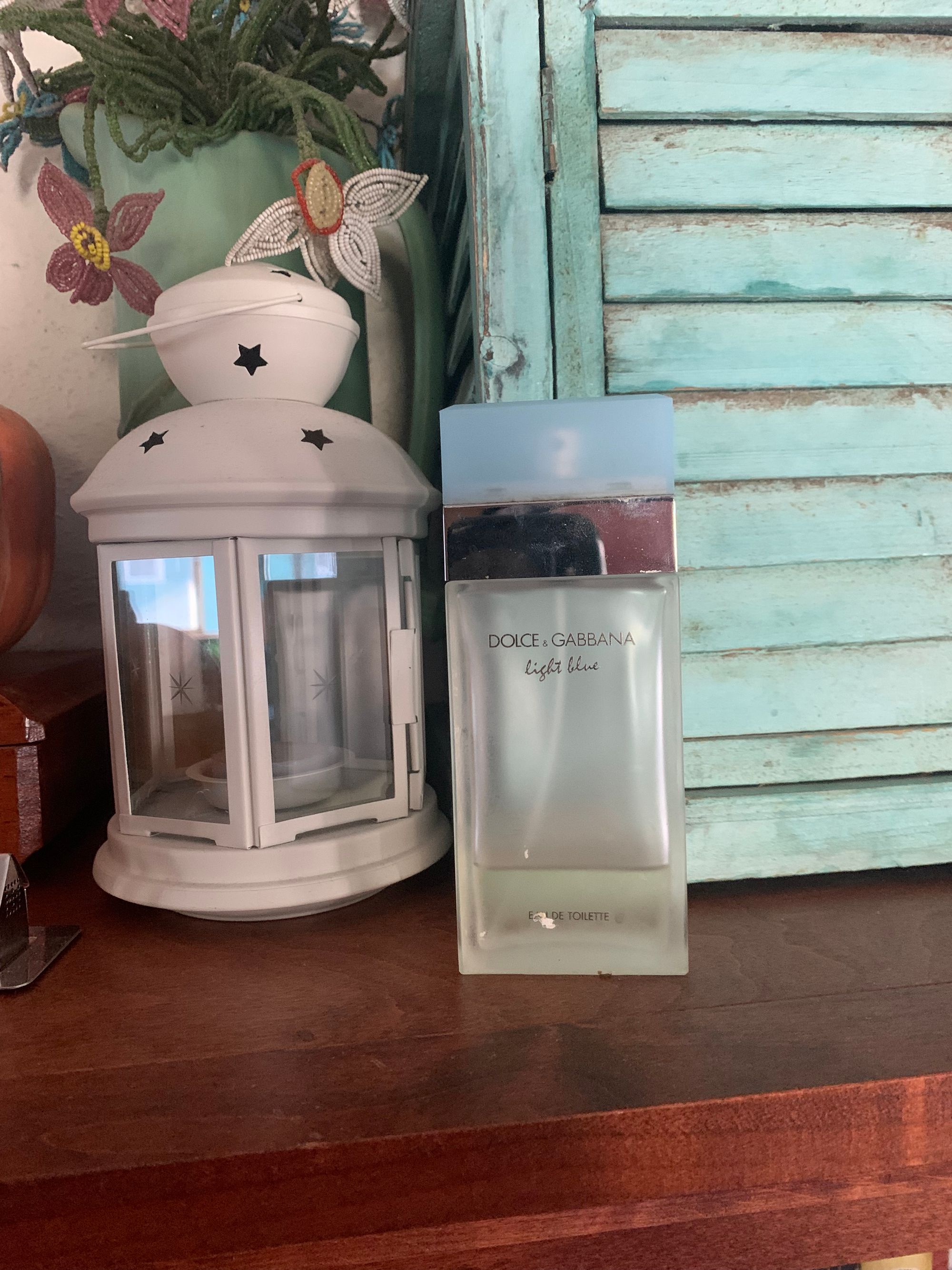 small white lantern, bottle of perfume, beaded flowers on a shelf