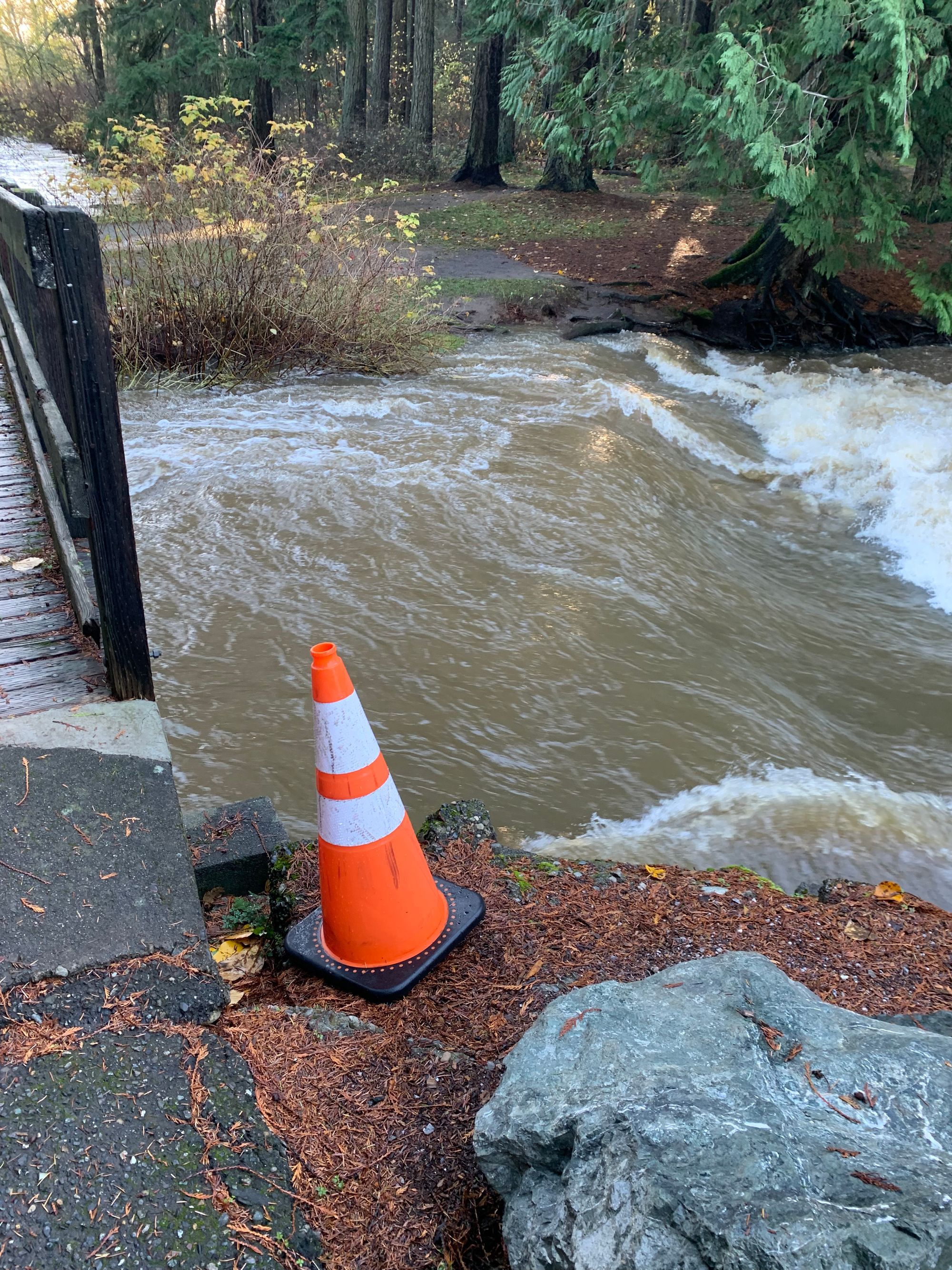 an orange cone next to a wooden bridge, a very full creek