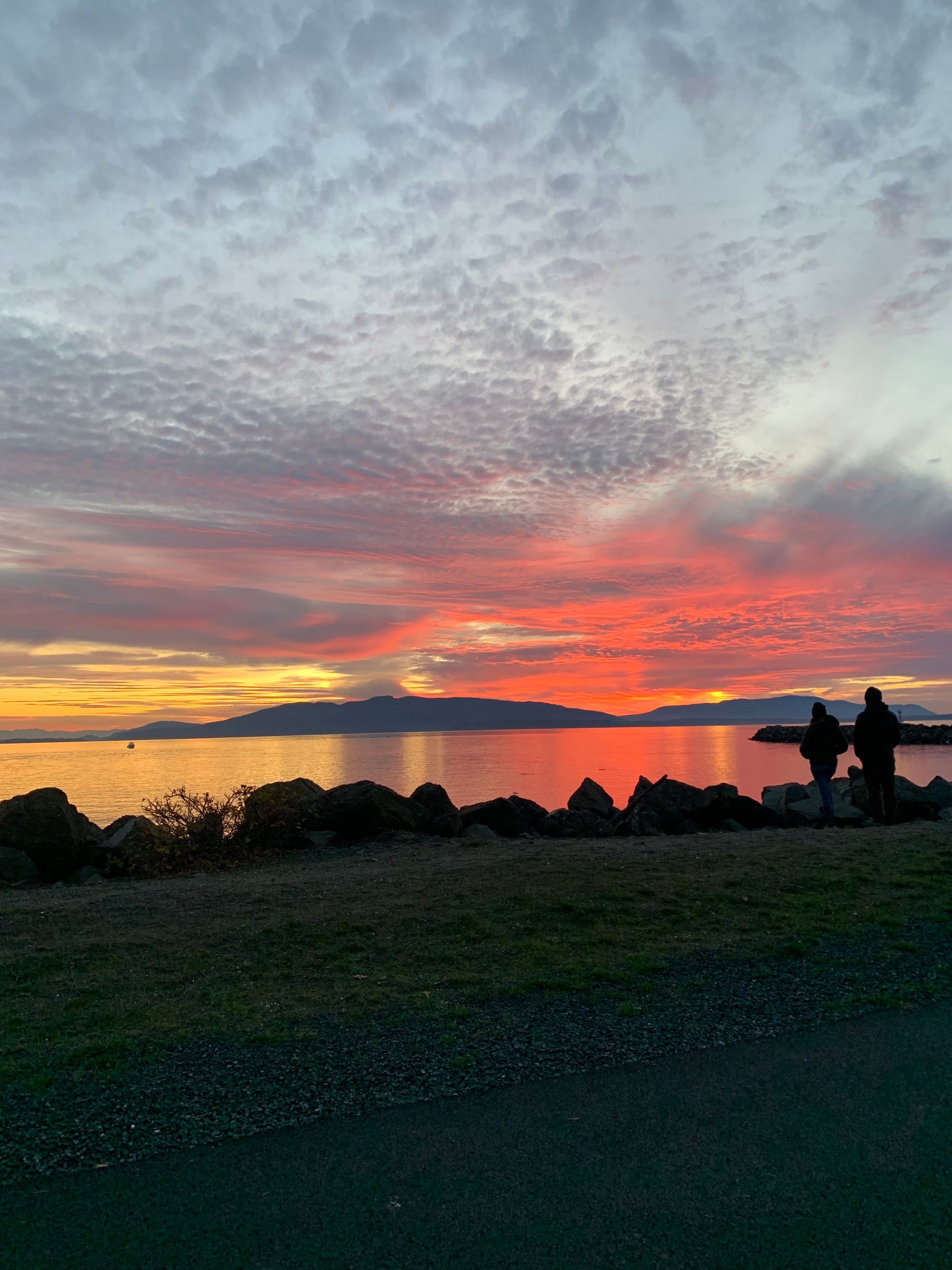 sunset over bay, pink and orange clouds, two human figures