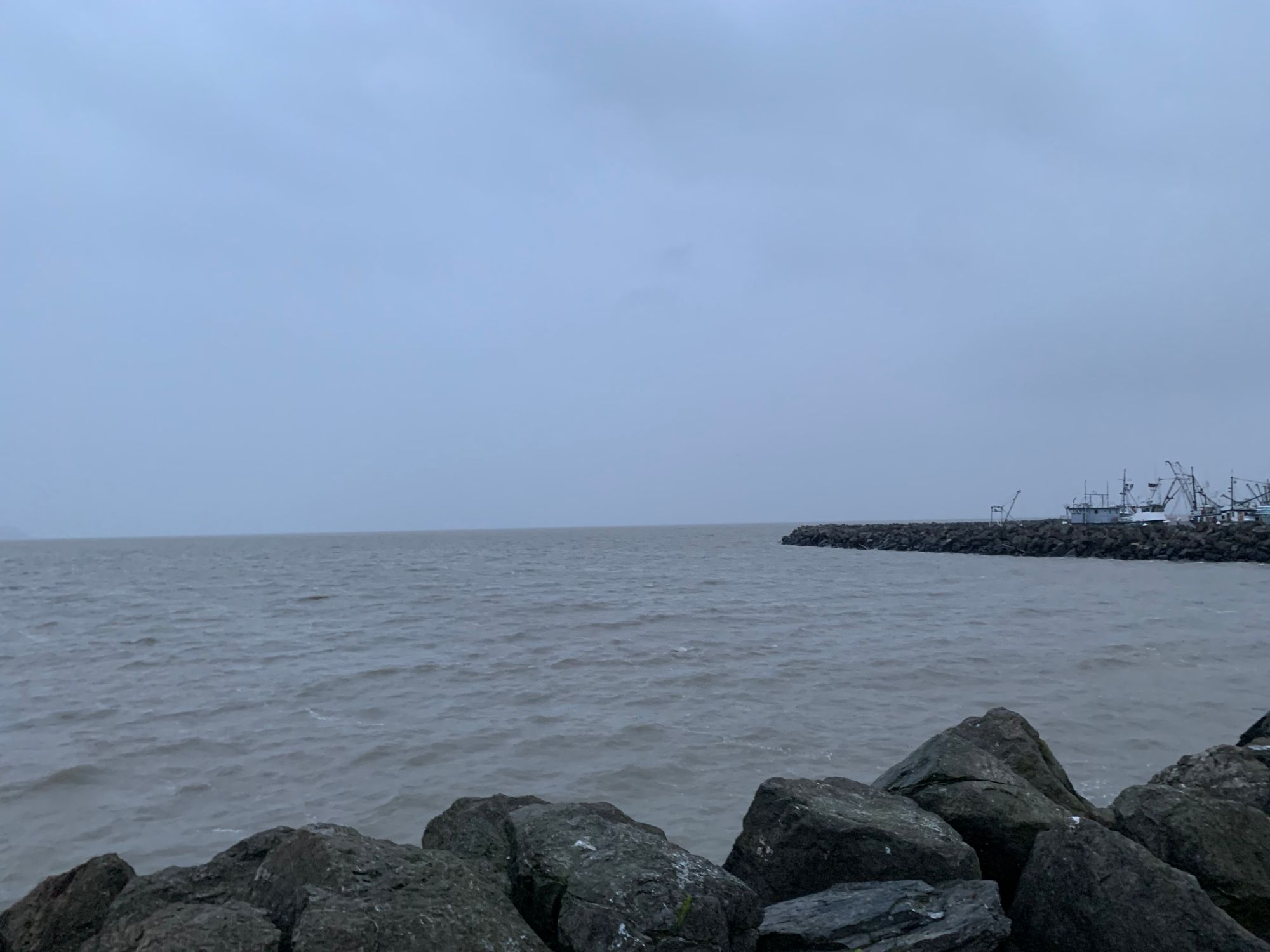 grey sky, water & rocks, a few boats in the harbor