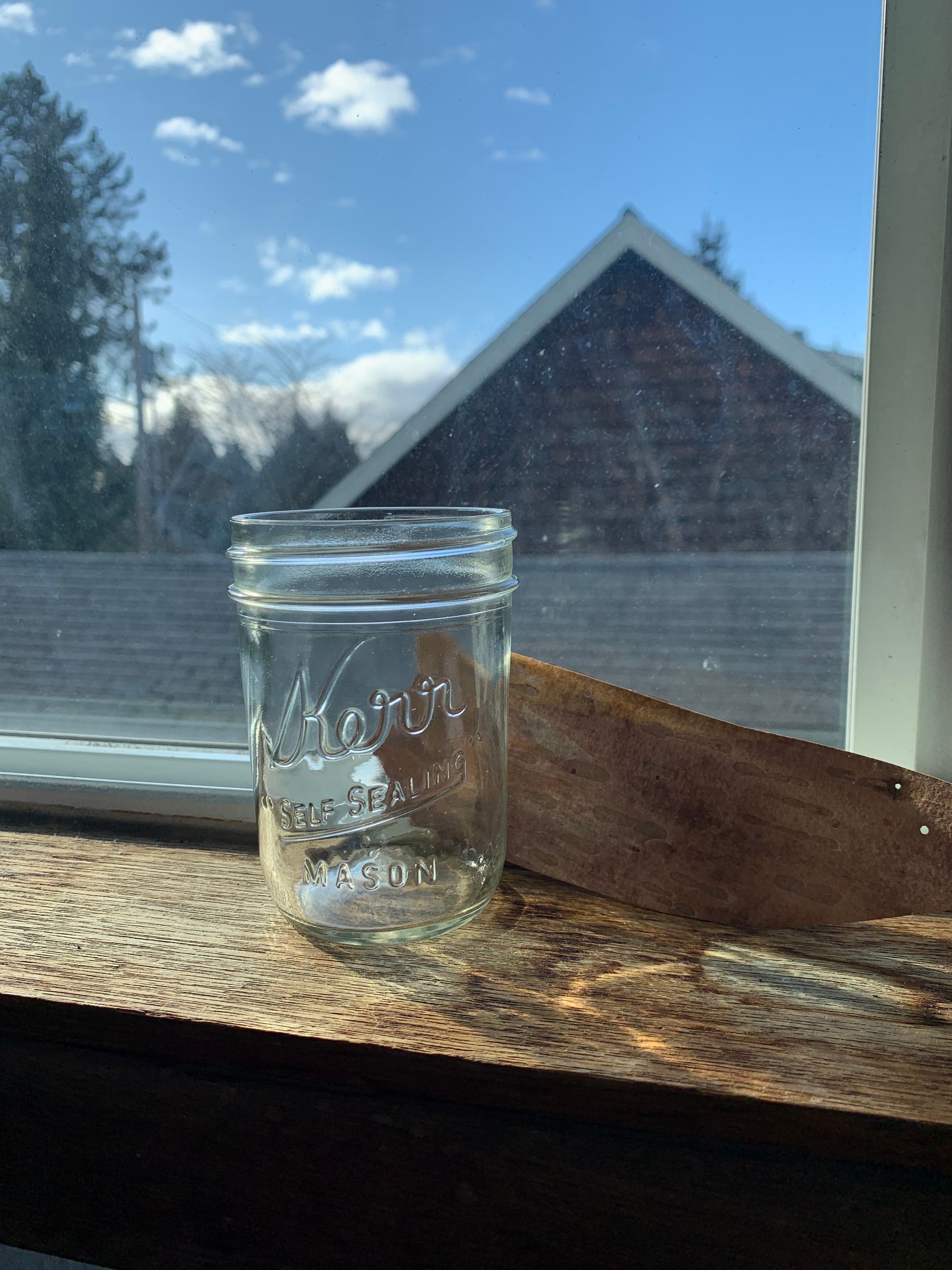 wooden windowsill, empty jelly jar, strip of birch bark, view of sky & rooftops