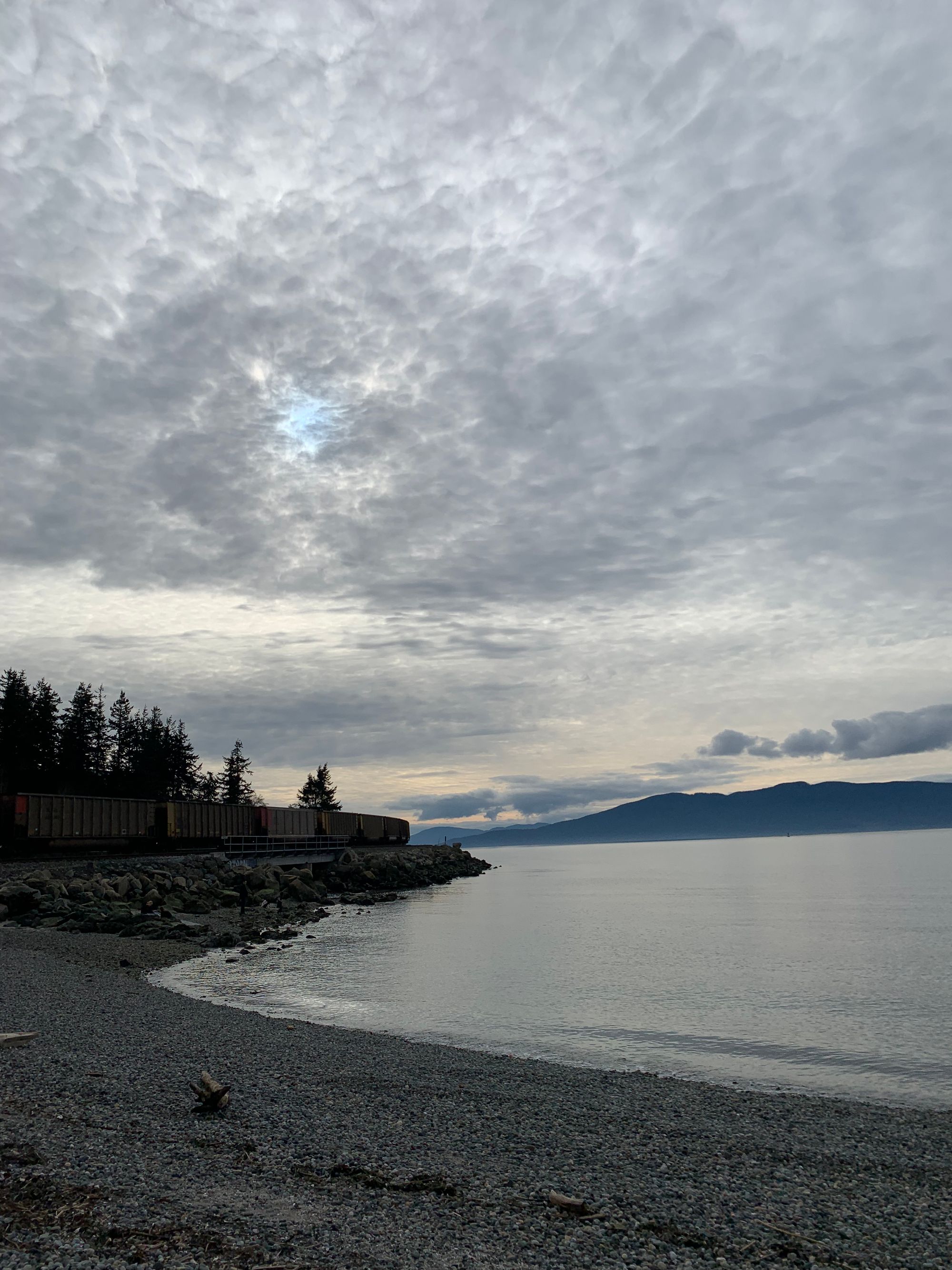 grey water, pebbly beach, islands & grey sky, train rounding a bend