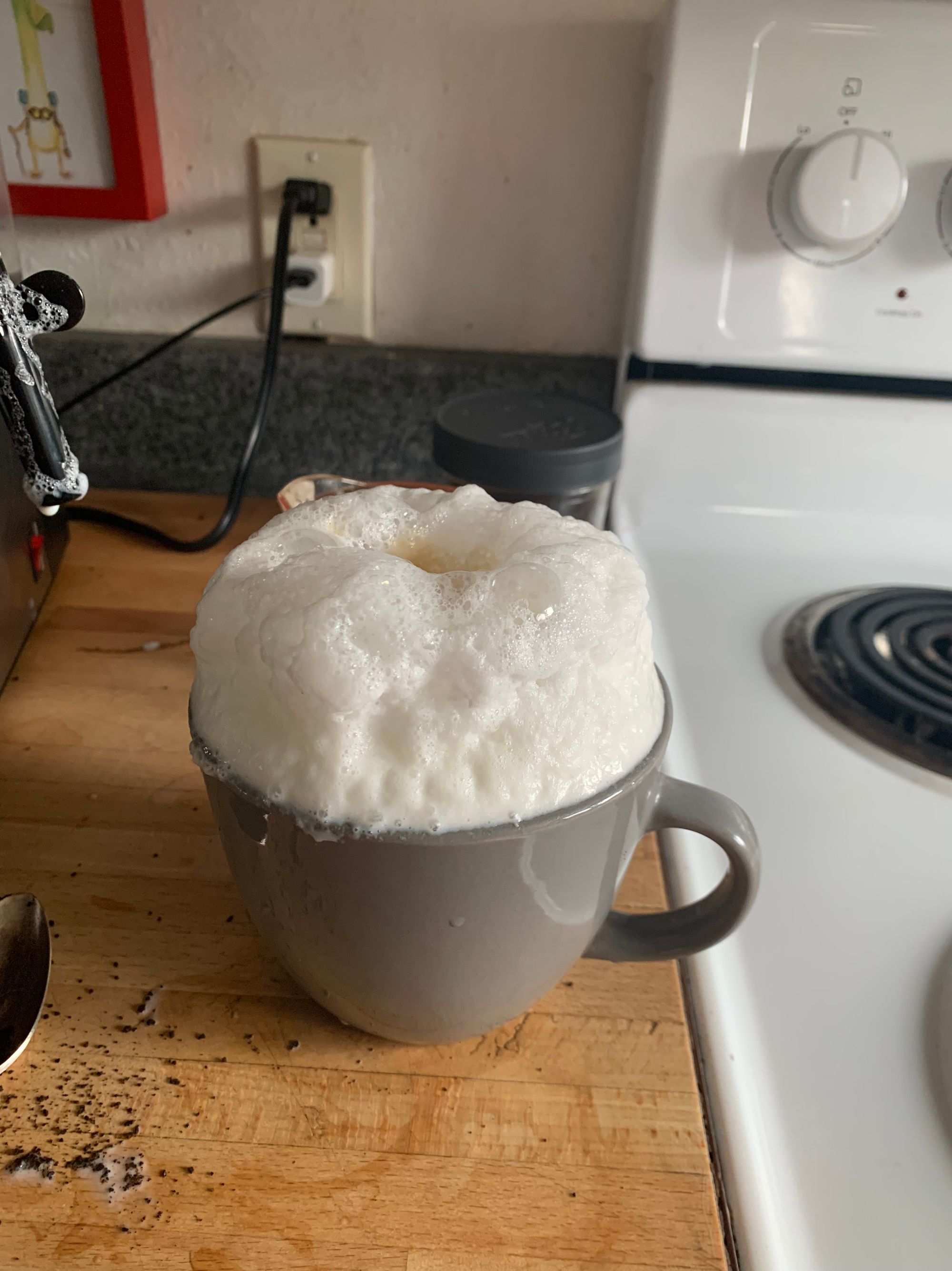 grey mug with overflowing milk foam on a wooden cutting board