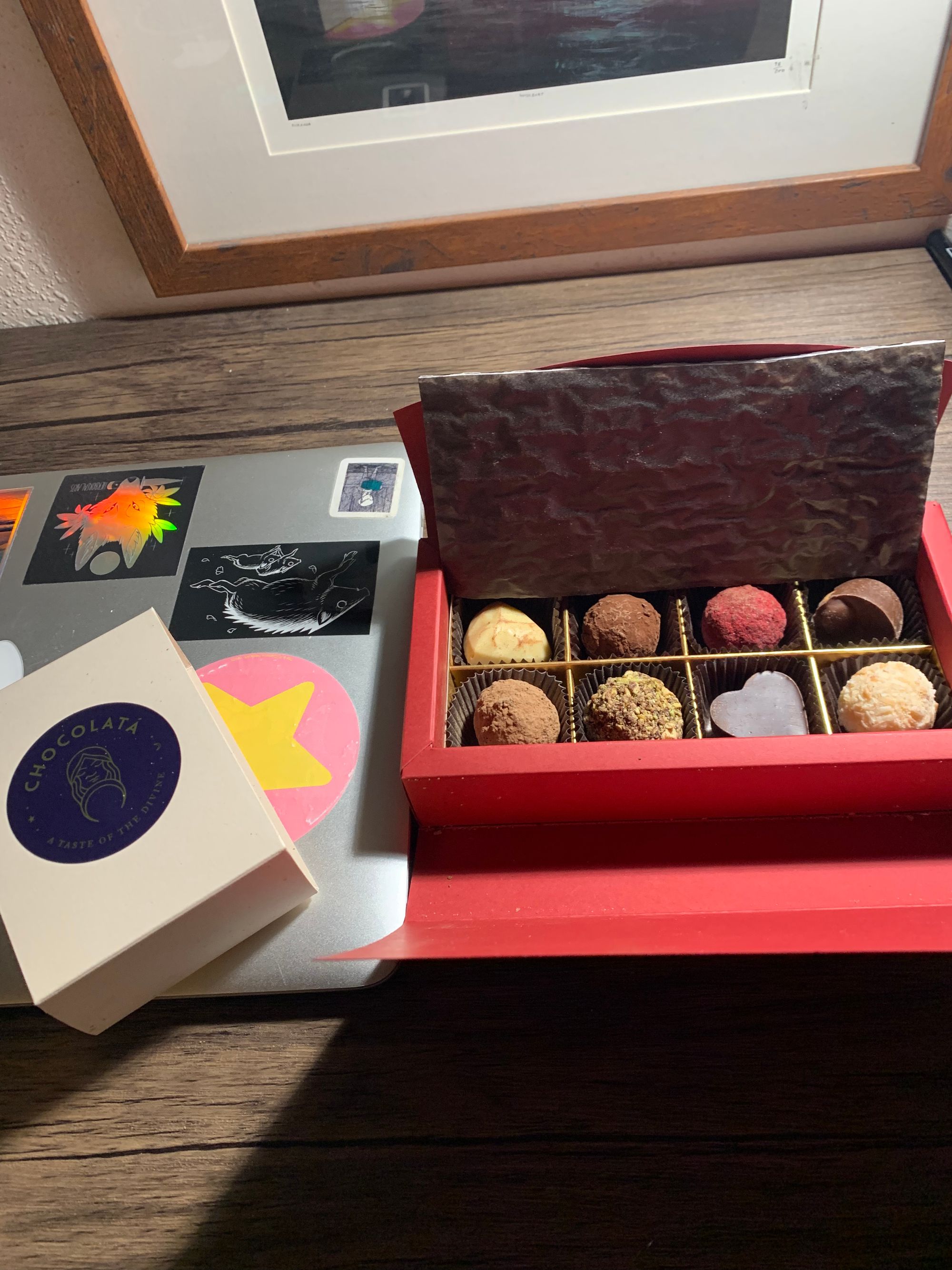 red box of very fancy truffles on a desk, chocolate wrapping label next to them, laptop underneath