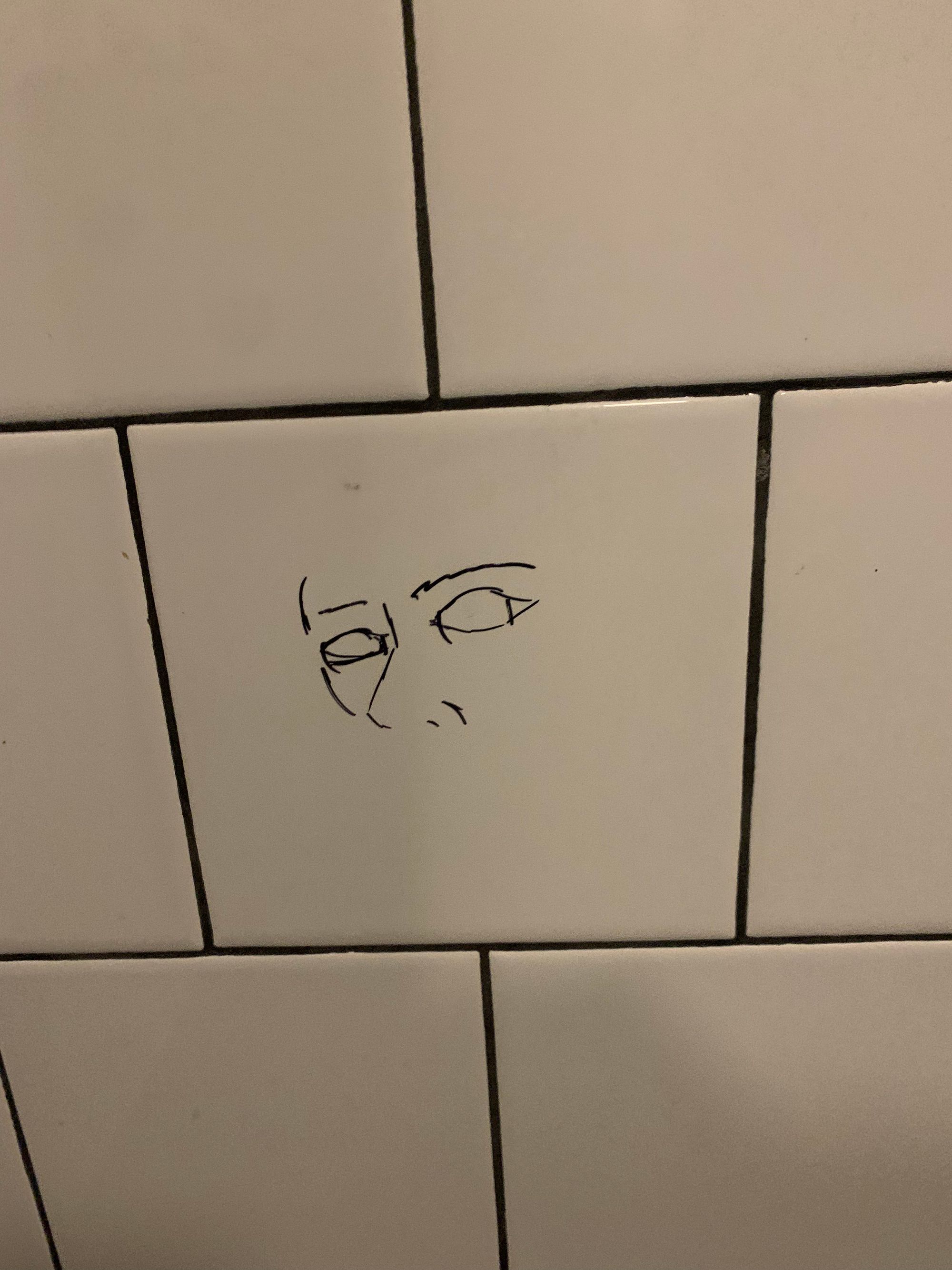 bathroom graffiti of a simple face in black marker on white tile