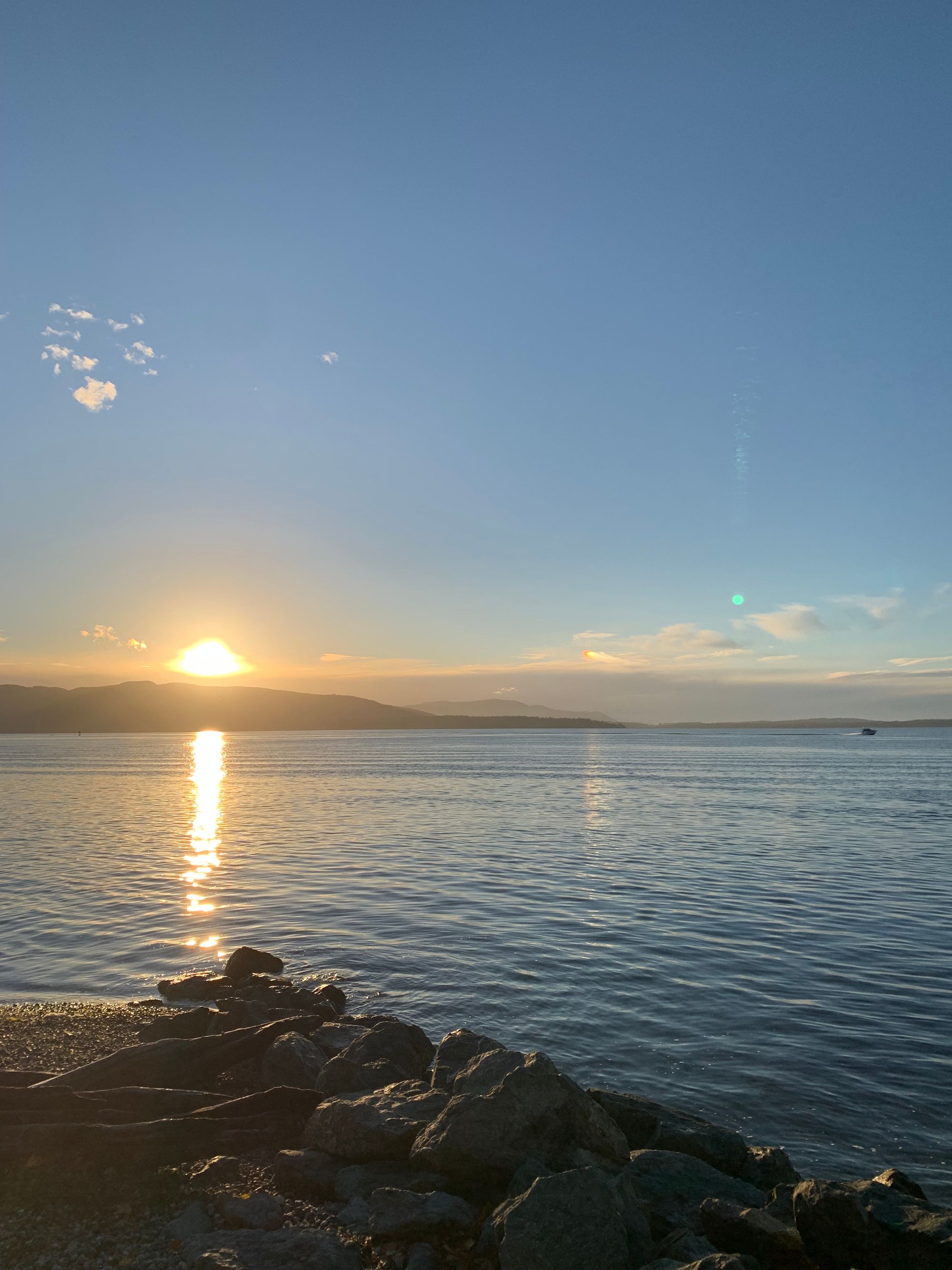 dark islands, blue water with setting sun & path of light across it, rocky beach