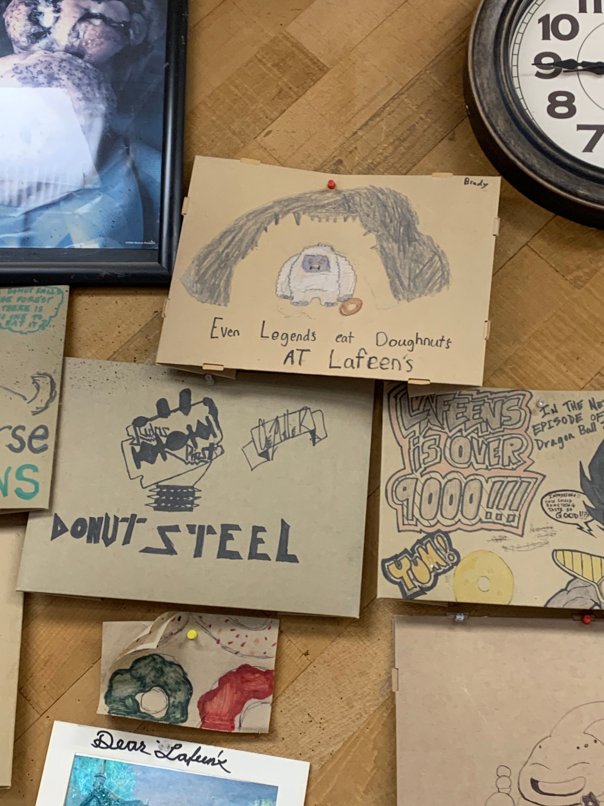 wooden wall with various cardboard signs, handwritten & hand drawn. the middle one says "even legends eat donuts at lafeens" with a drawing of a yeti.