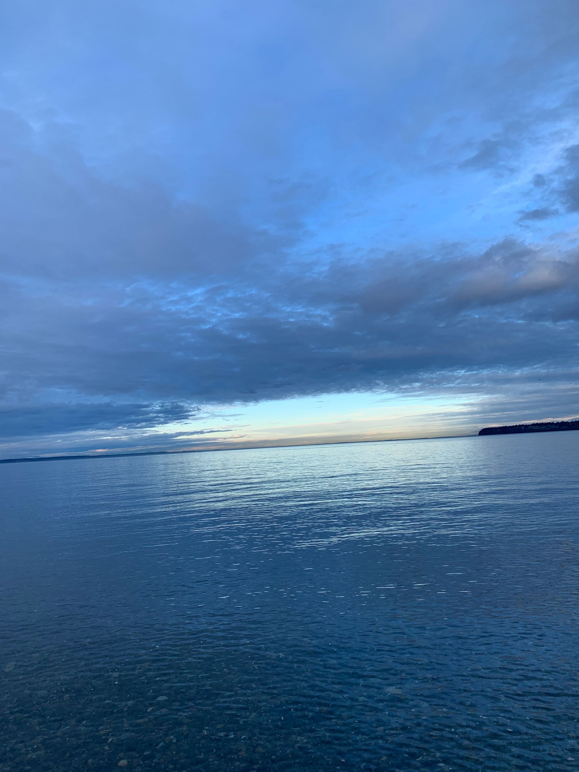 clear bright water, cloudy sky with a big bright break at the horizon where blue is visible, islands in the distance