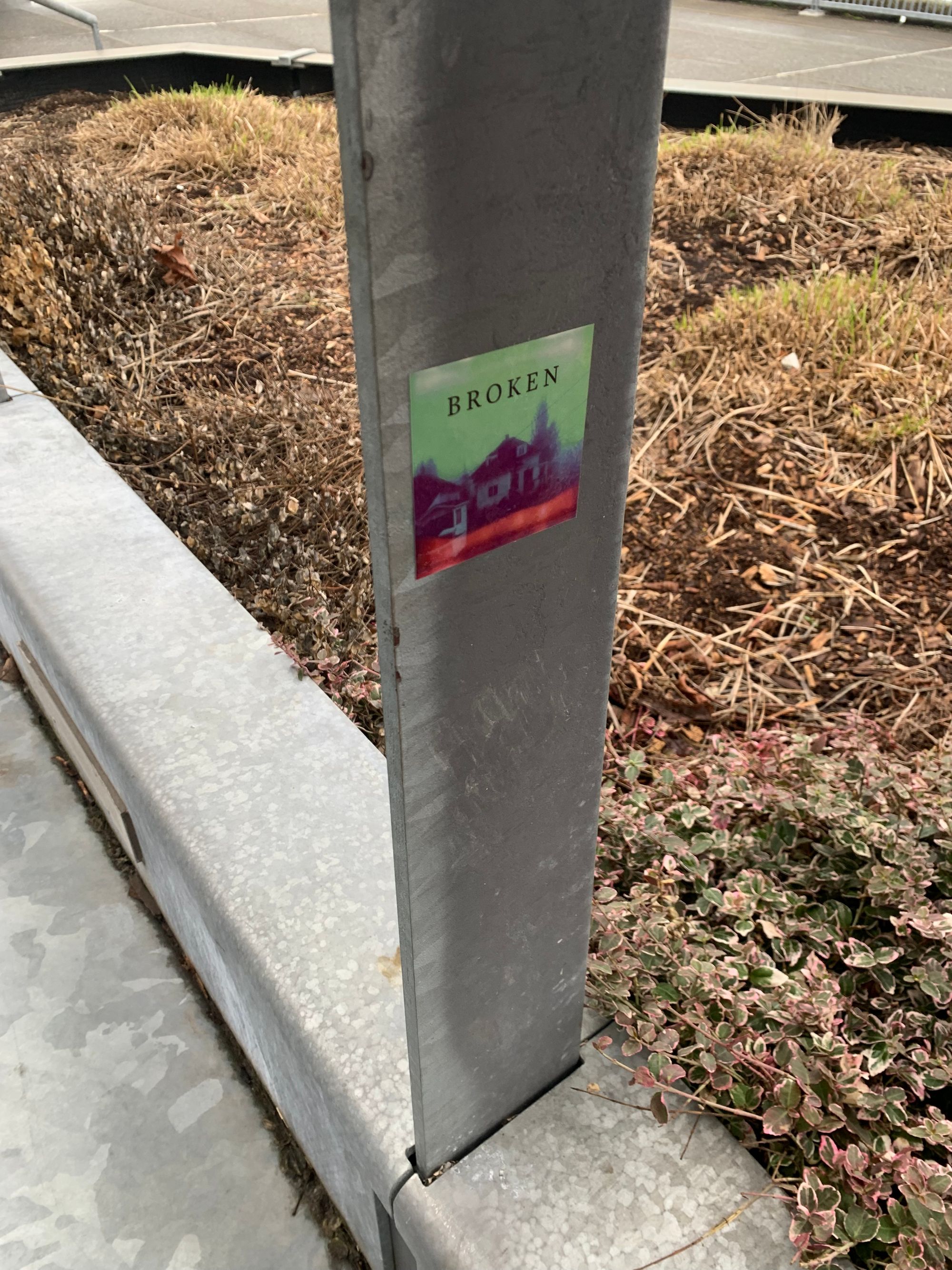 metal railing with a sticker showing a ghostly looking house with the word 'BROKEN' in all cap above it