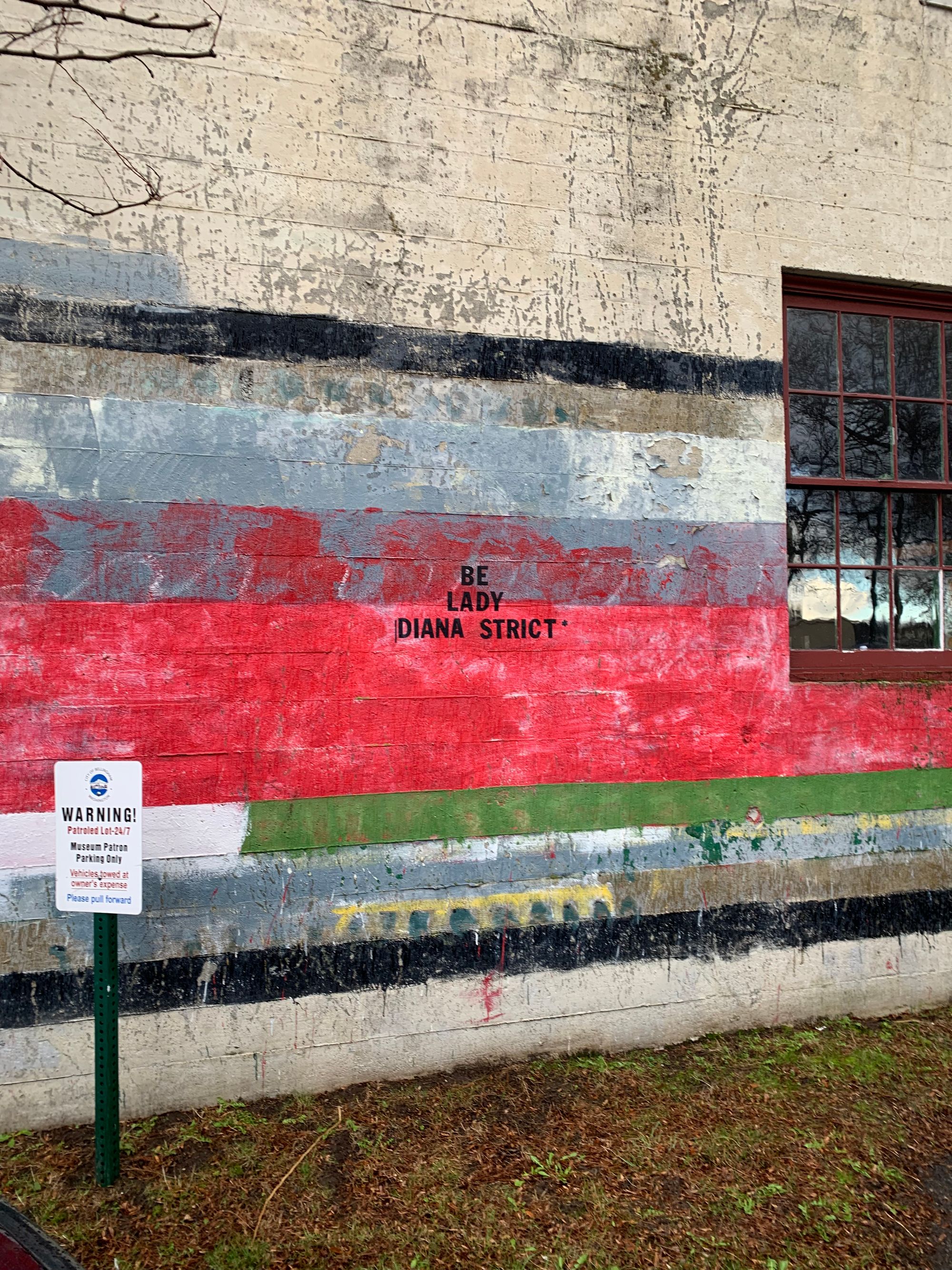 white brick wall with stripe of red paint & stencil letters that read: BE LADY DIANA STRICT