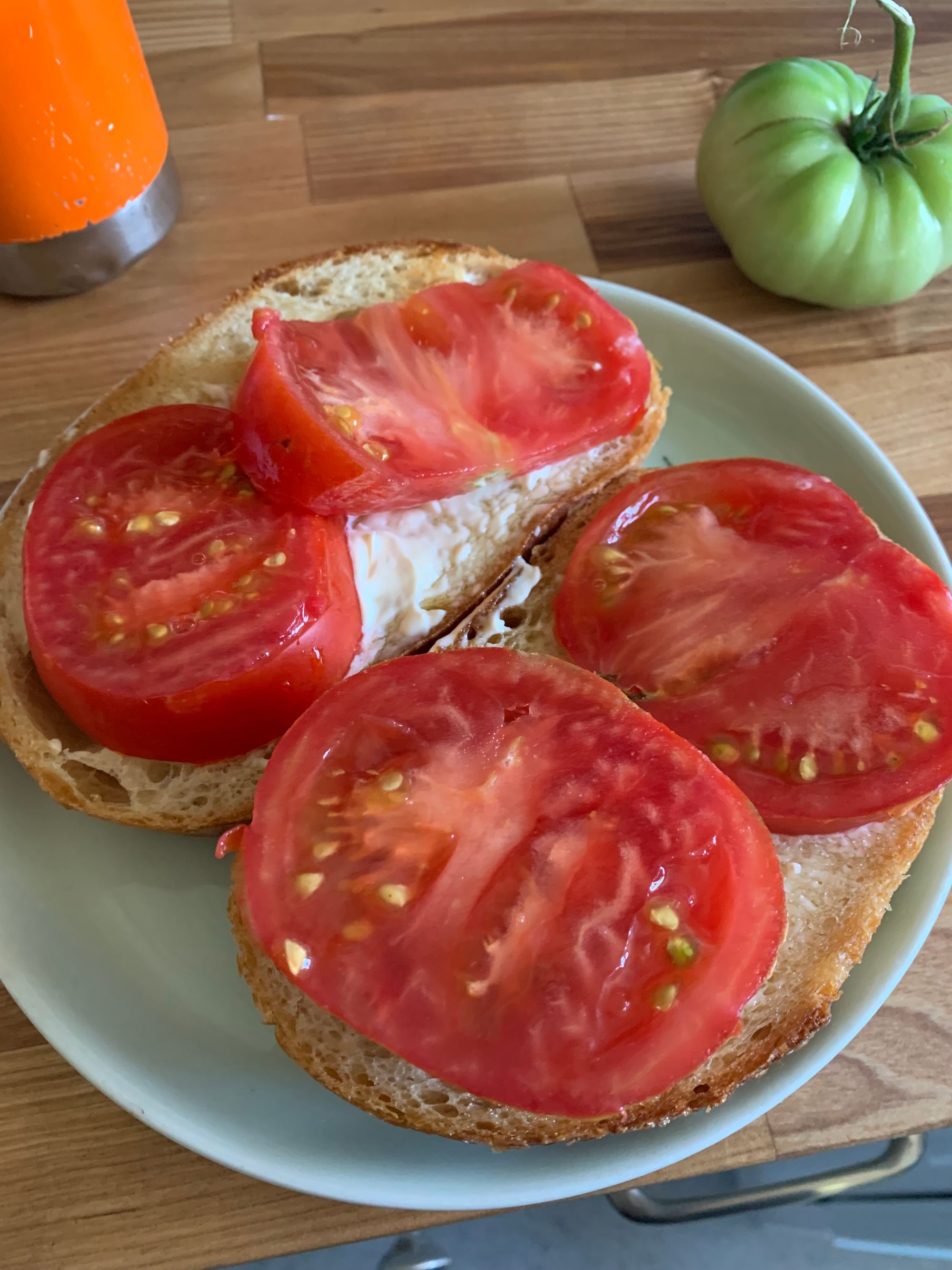 a tomato sandwich on thick bread on a light blue plate, an orange water bottle & green unripe tomato in the background