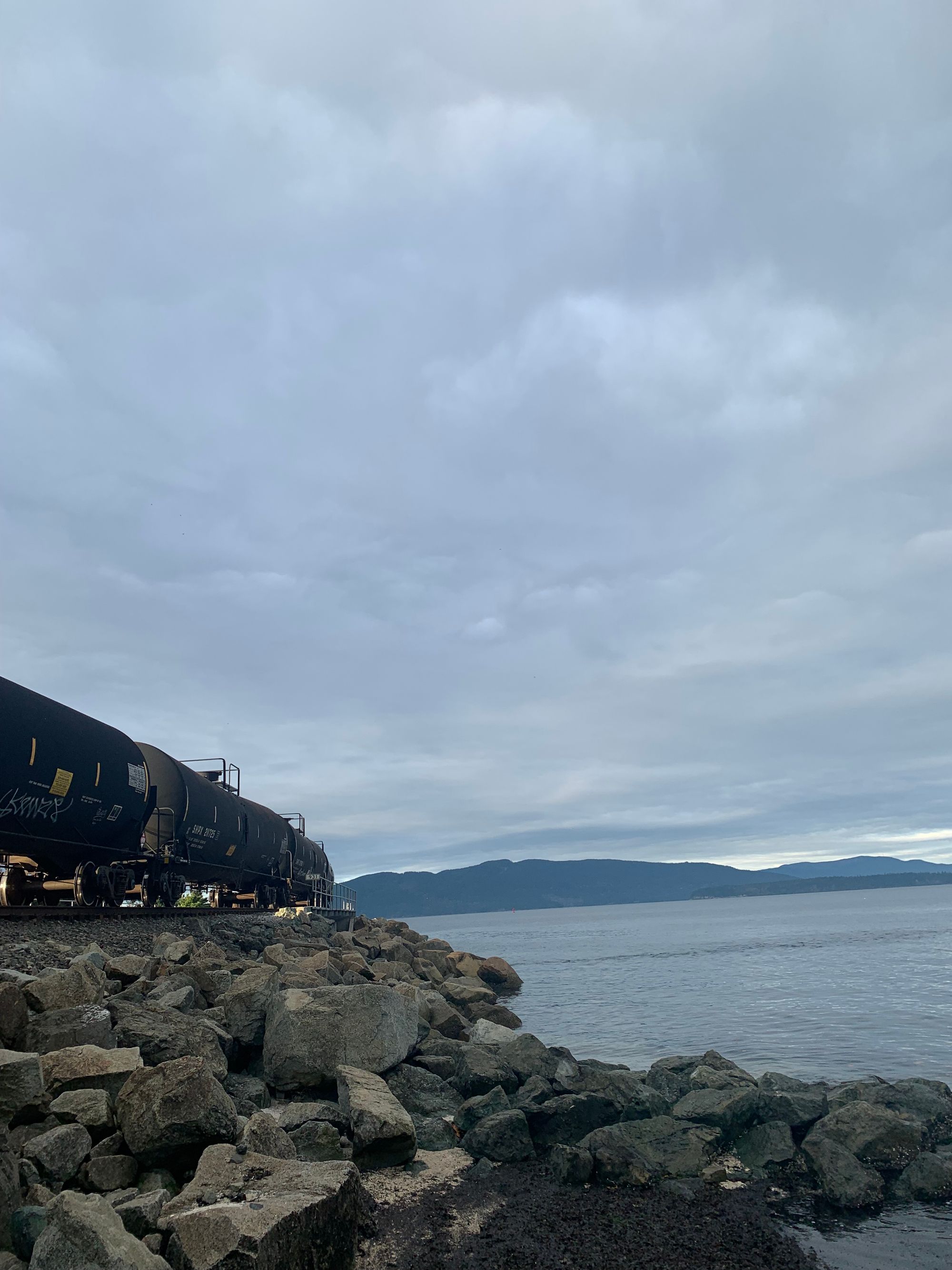 rocky shore, black tank cars on train tracks, islands in the distance, grey water