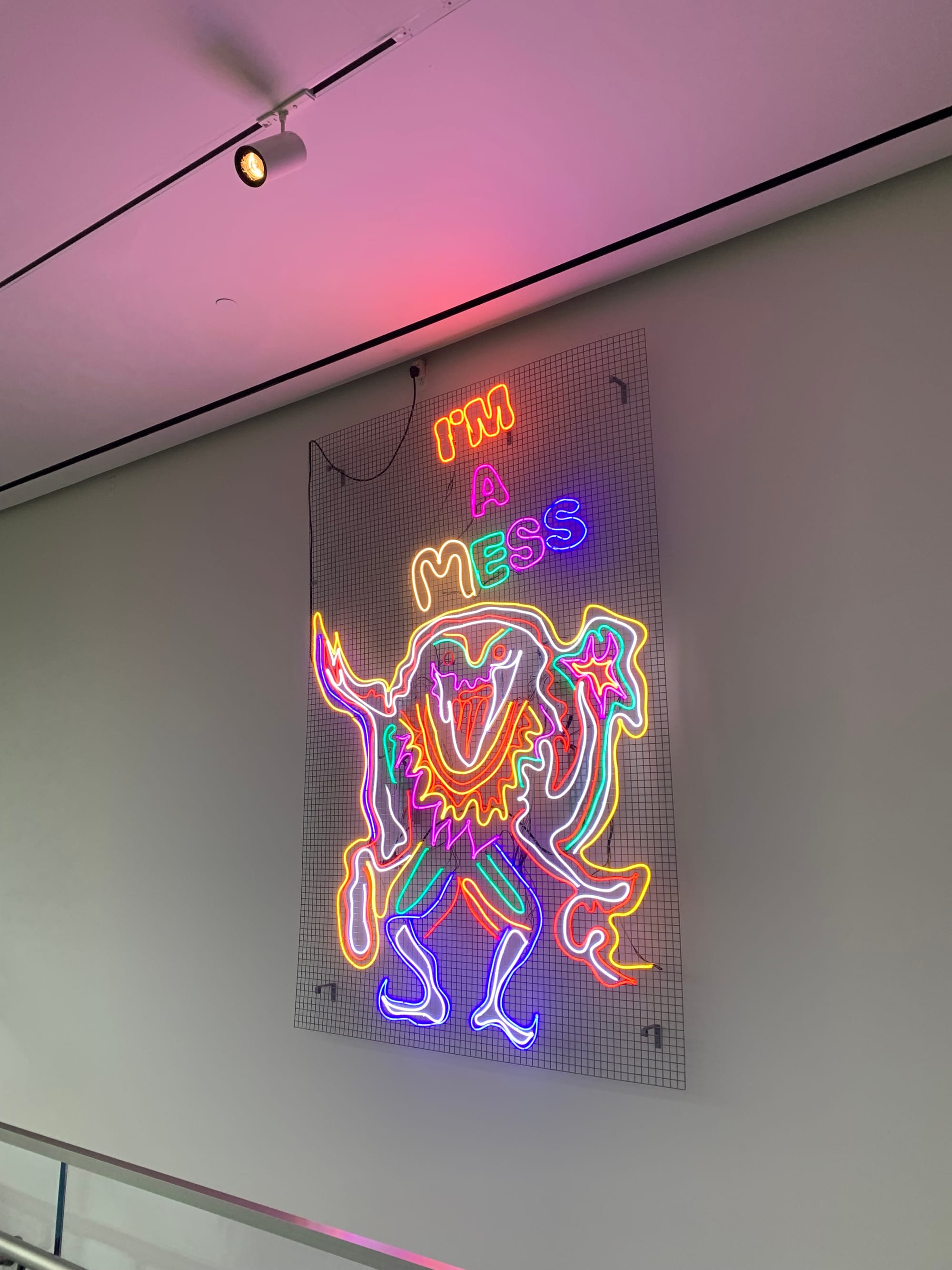 neon art on a white wall, with lettering saying, "I'm a mess" & an abstract humanoid figure