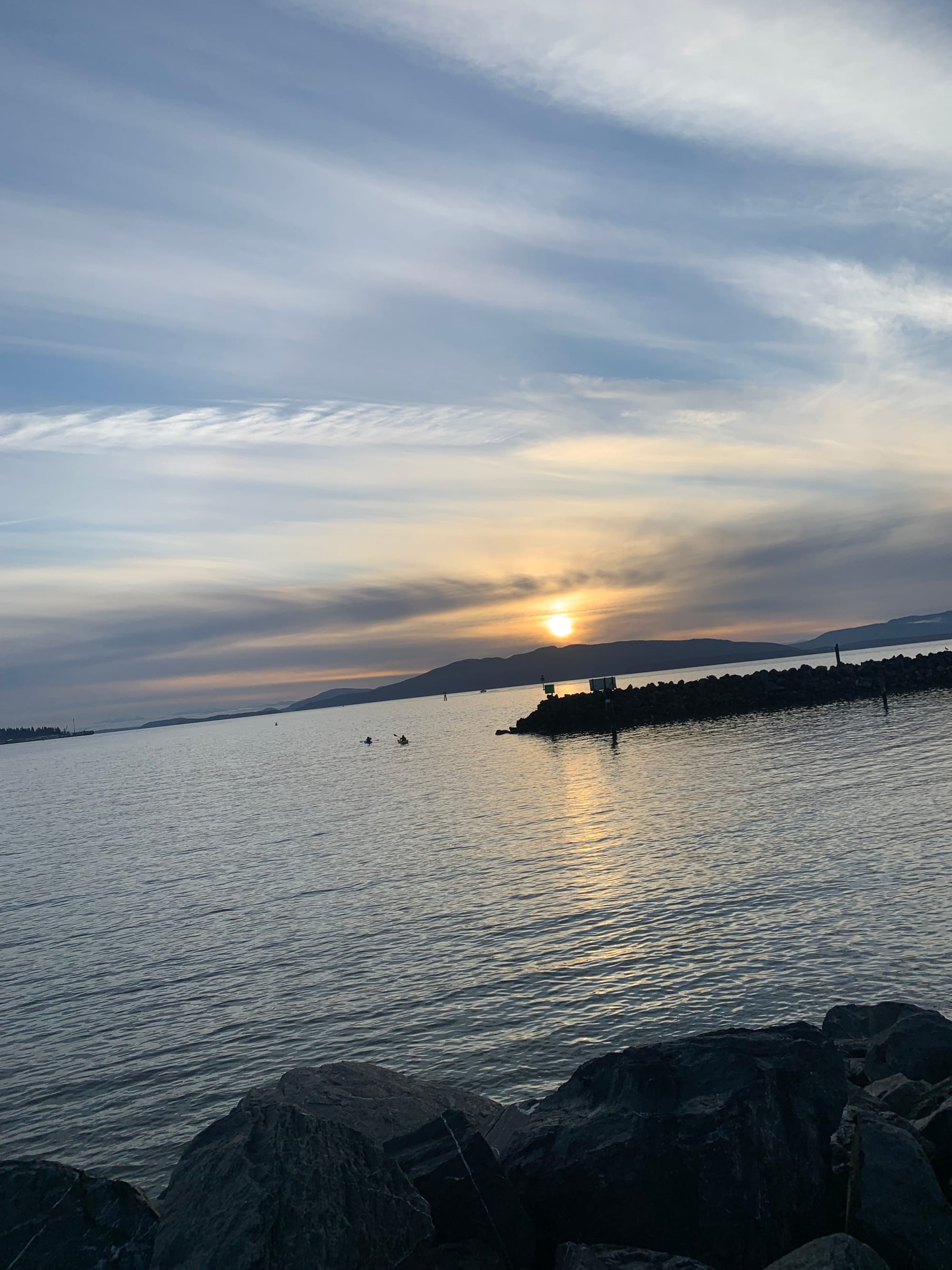 sunset over islands, a rock jetty, grey water, peach and grey clouds