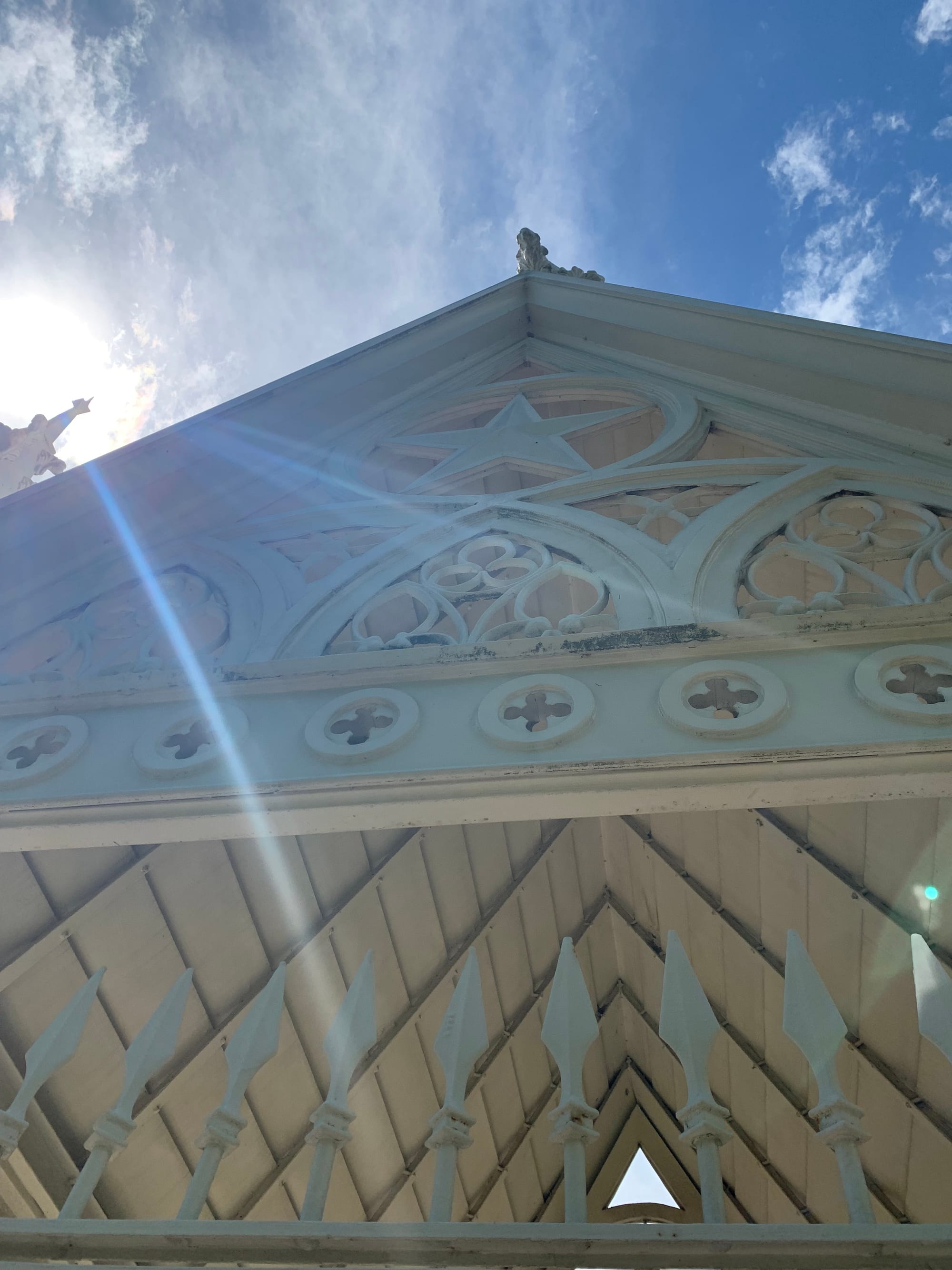 the peak of an ornate white building against a blue sky, sunbeams coming down across the photo