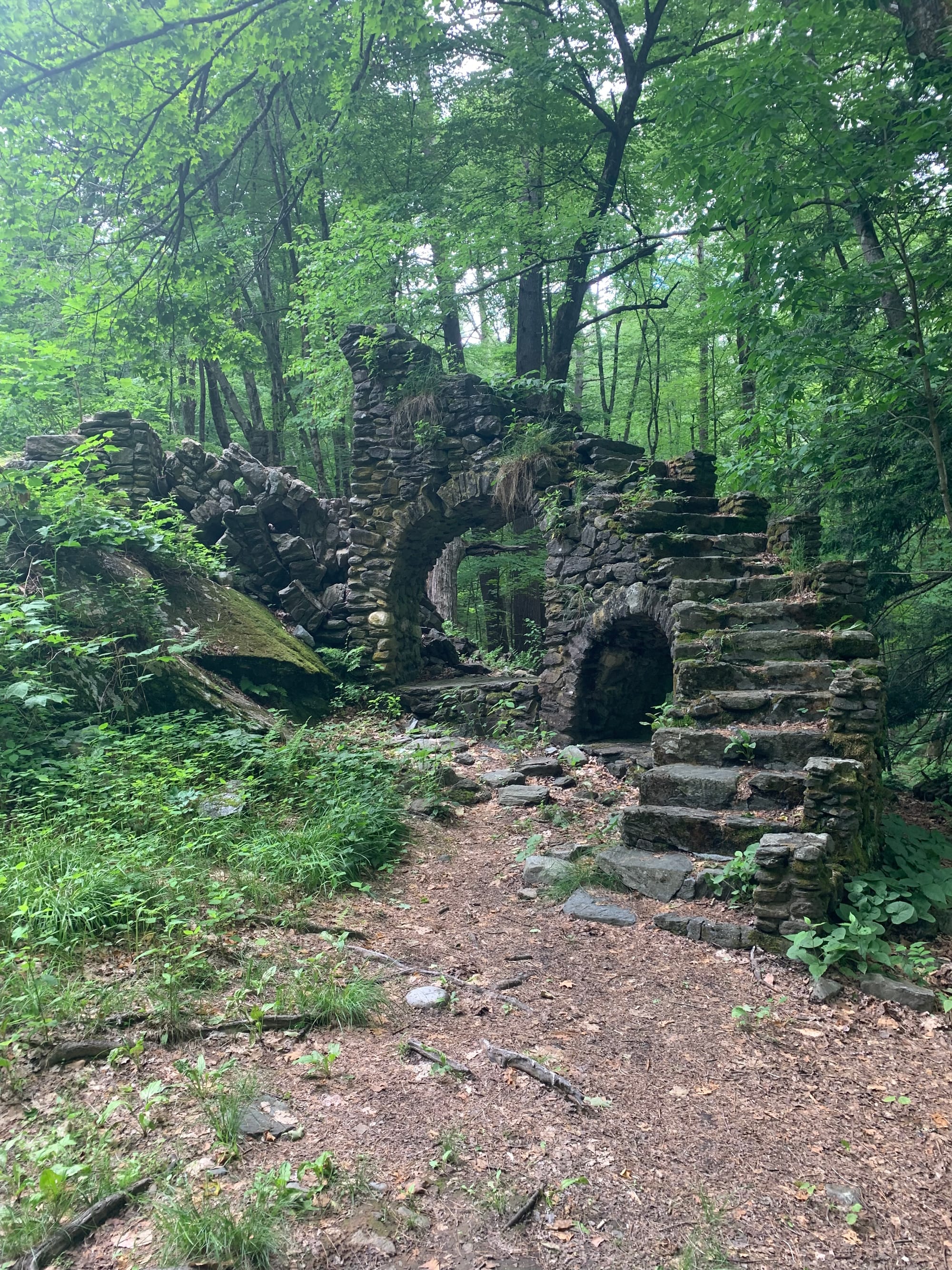 tumbling down rock walls & archway, stairs ascending to a fallen arch, surrounded by green trees