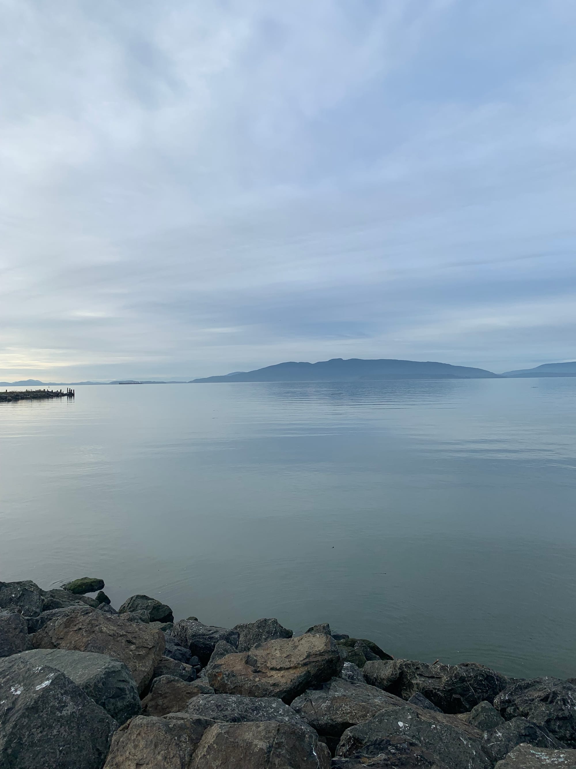 thin grey scrim of clouds, islands in the distance, nearly glassy water, rocks in foreground