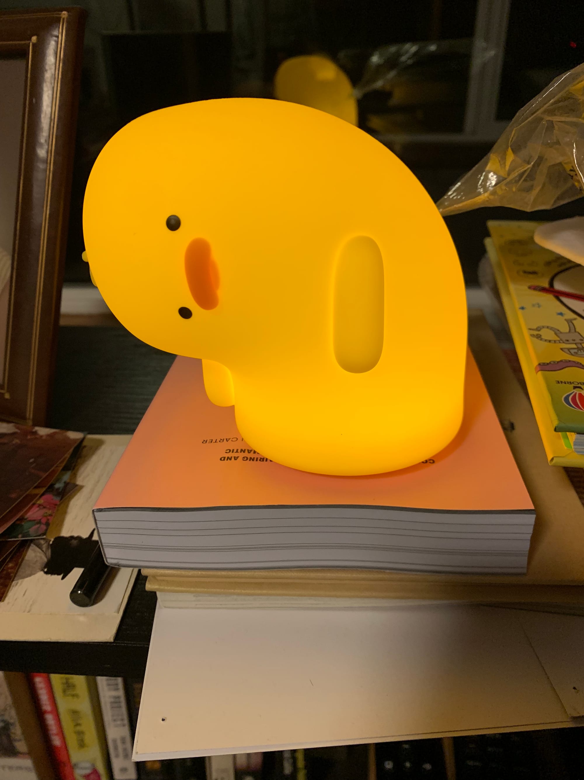 small yellow duck lamp, in which the duck's head is bent to the left at a 90 degree angle, on a stack of books