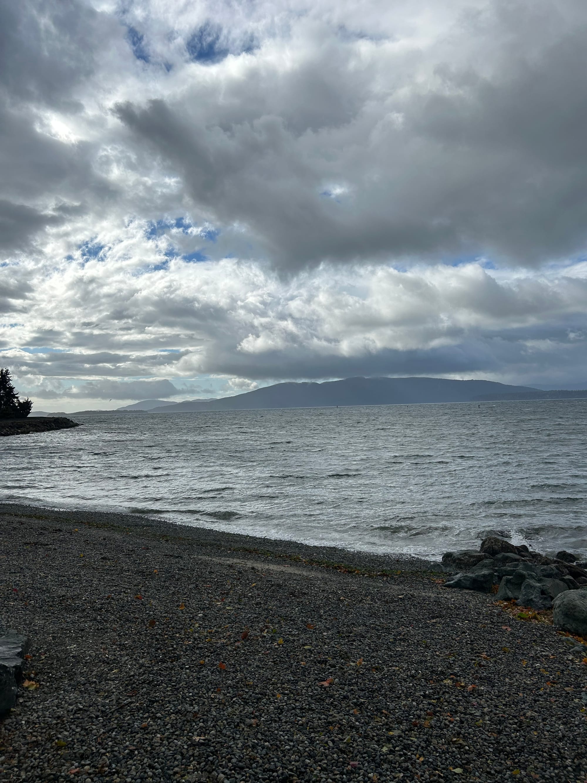 islands in the distance, pebble beach, shining grey water, cloudy with peeks of blue overhead