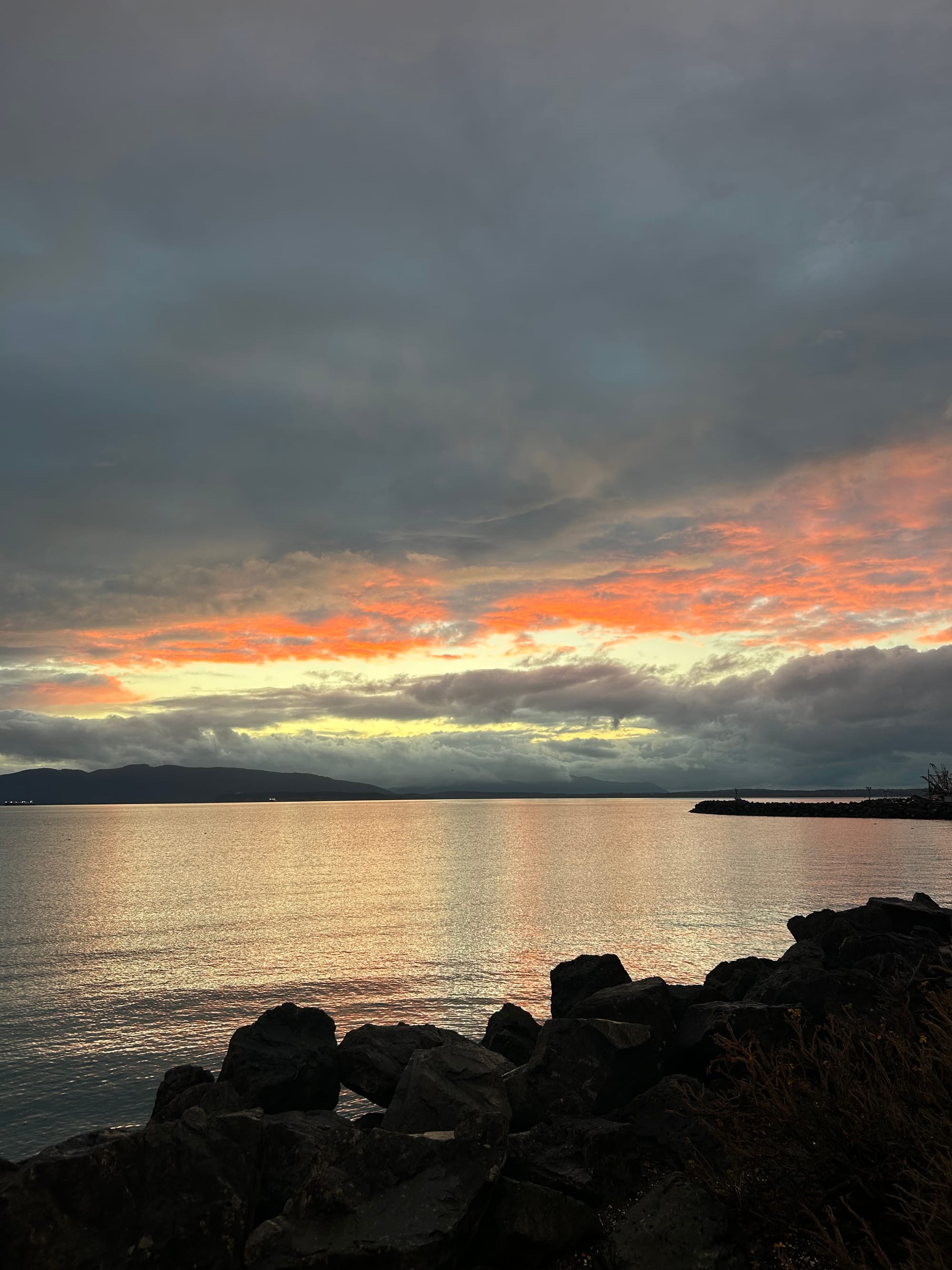 a pink and grey sunset with a low cloud bank over silver water